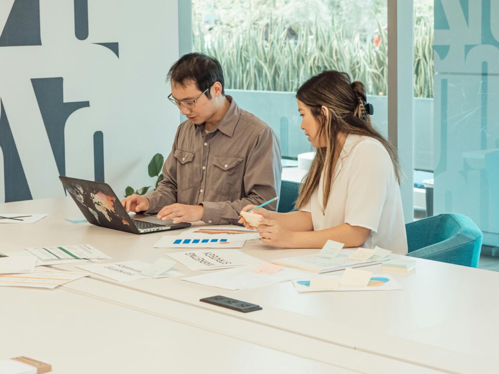 Two colleagues collaborating in a modern office setting over a laptop and documents.