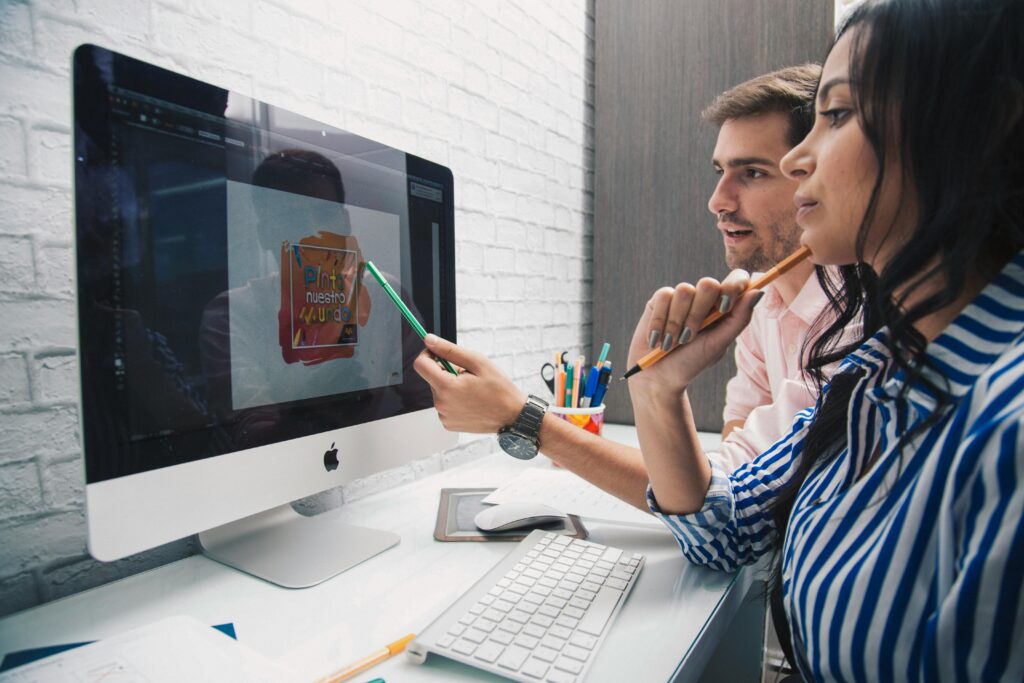 Side view of focused coworkers working together on graphic design while sitting at table and looking at monitor in modern office